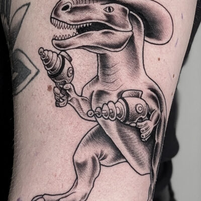 Tatuointi jossa dinosauruksella on stetson-hattu ja laser-pistoolit käsissä. Tyyli old school ja tatuoija Bryan Scott Leima-tatuointiliikkeestä.